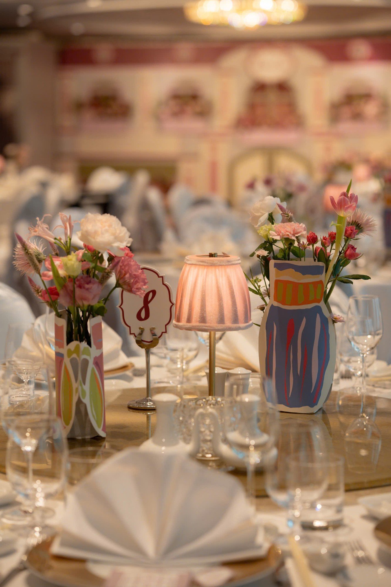 Centerpiece thực tế với đèn bàn hồng, số bàn 8 và hai bình hoa vẽ tay